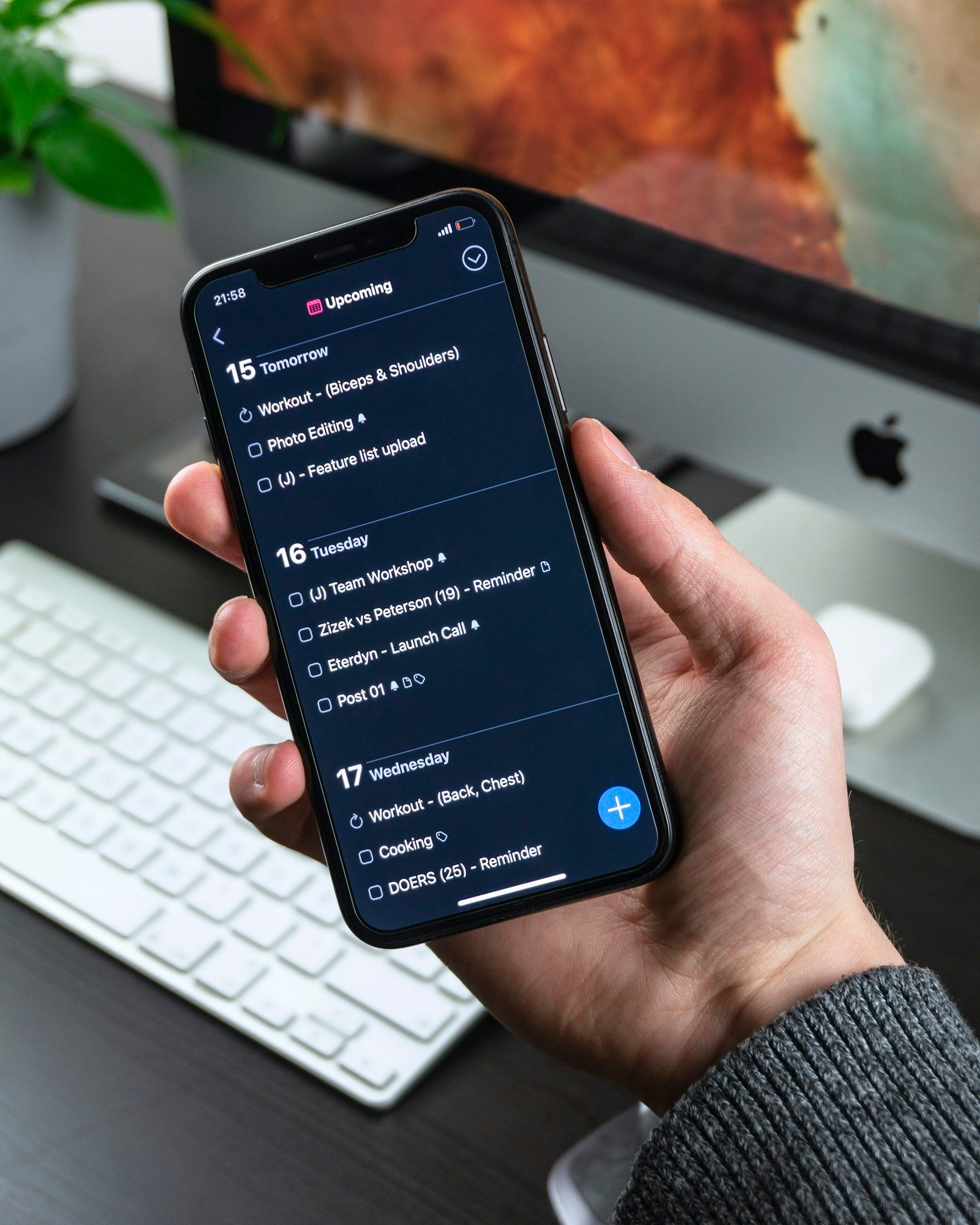 Person holding an iPhone with a dark productivity app in a workspace