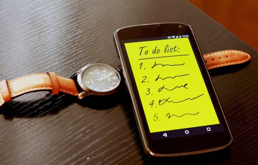 Smartphone showing a simple to-do list beside a watch on a desk